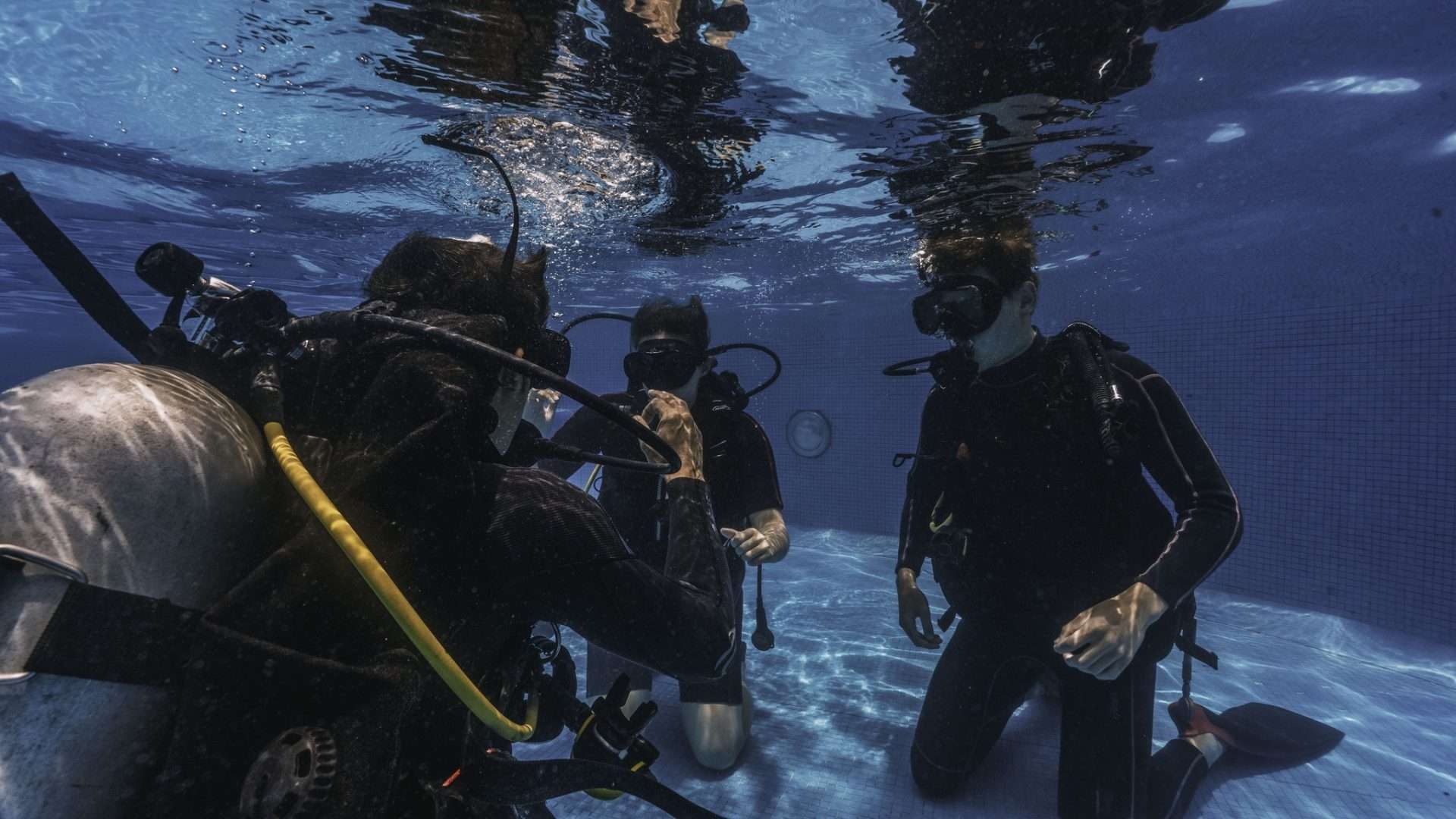 diving instructor teaches students to scuba dive in swimming pool. couple getting first experience with scuba diving under the guidance of experienced recreational diving instructor on vacation.
